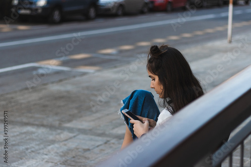 woman waiting for the bus, looking at the mobile phone, sitting on a bench