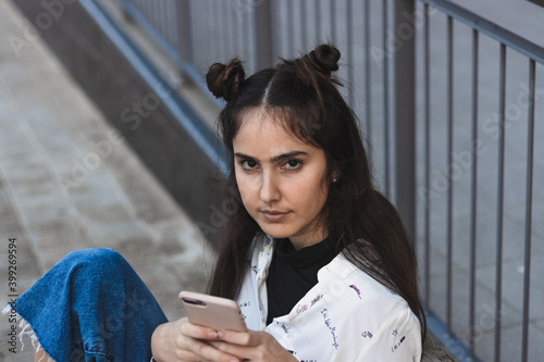 woman waiting for the bus, looking at the mobile phone, sitting on a bench