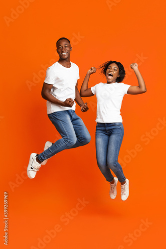 Cheerful african american couple clenching fists and jumping up
