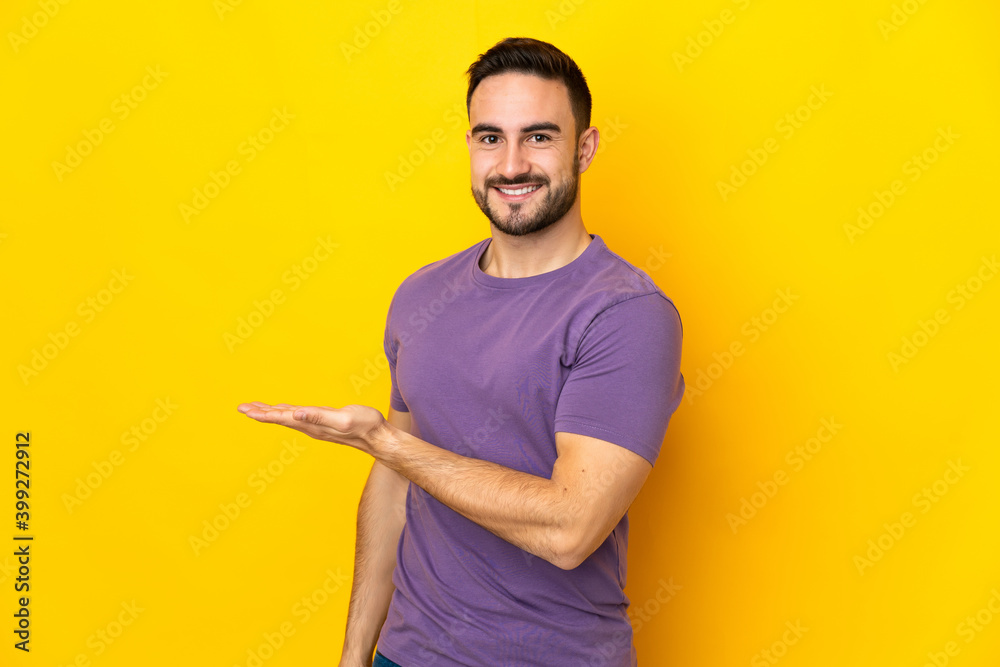 Young caucasian handsome man isolated on yellow background presenting an idea while looking smiling towards Young caucasian handsome man isolated on yellow background presenting an idea while looking smiling towards