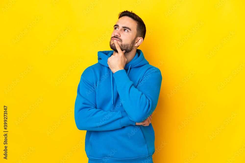 Fototapeta premium Young caucasian handsome man isolated on yellow background having doubts while looking up