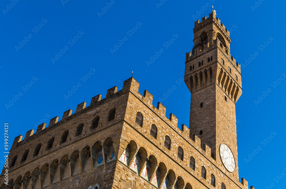 Great close-up corner view of the famous cubical Palazzo Vecchio museum with the clock on the Arnolfo’s tower (Torre d'Arnolfo) in Florence, Italy. The façade is made of solid rusticated stonework.
