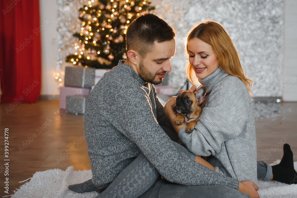 attractive cheerful man and woman sitting near christmas tree hugging. couple cuddling near christmas tree. New year's eve