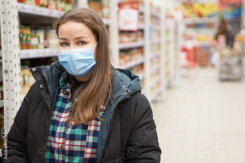 Portrait of Caucasian woman wearing medical mask, standing in hypermarket, warm clothes, copyspace