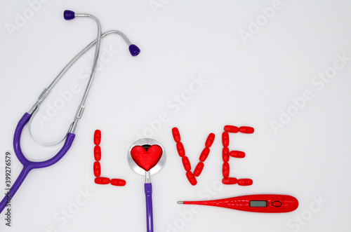 The word love is made of red pills and a stethoscope with a heart, thermometer on a white background with a copy space. Concept of Valentines day, medical flatly.