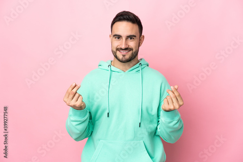 Young caucasian handsome man isolated on pink background making money gesture © luismolinero