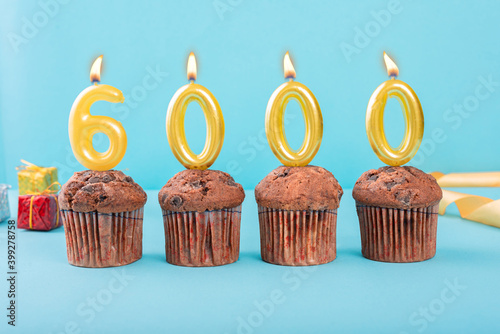 6000 Number gold candle on a cupcake against a pastel blue background six thousand year celebration