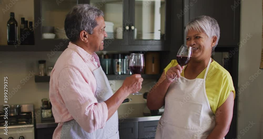 Happy senior mixed race couple wearing aprons toasting with wine in kitchen Happy senior mixed race couple wearing aprons toasting with wine in kitchen