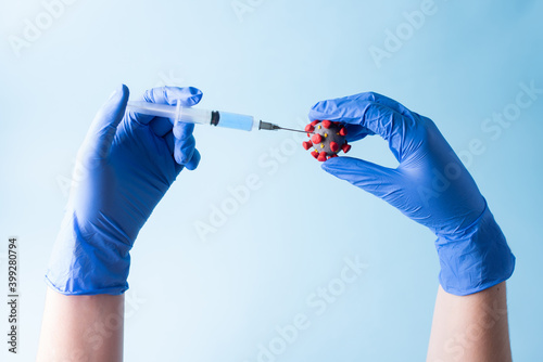 Hands in blue medical gloves inject a syringe into coronavirus ball model.