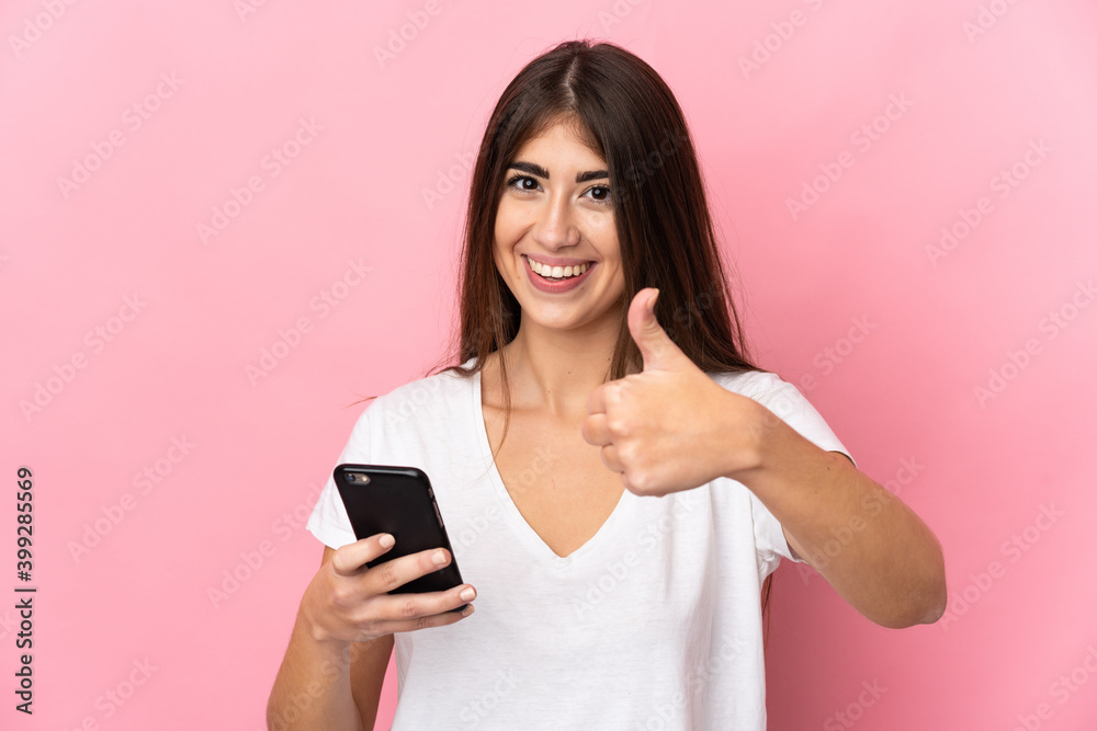 Young caucasian woman isolated on pink background using mobile phone while doing thumbs up Young caucasian woman isolated on pink background using mobile phone while doing thumbs up