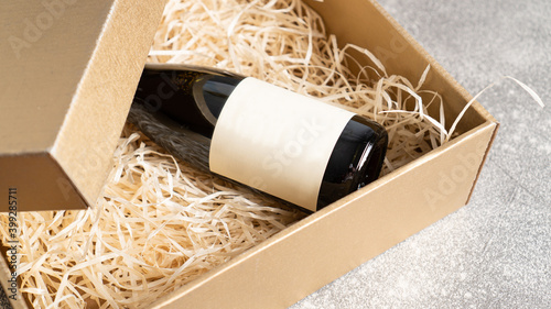 Present box with a bottle of wine with a blank label. Birthday present. Wine bottle in a wooden box with hay