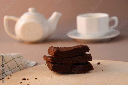 Chocolate brownie on wooden board with a teapot and cappuccino. Bokeh photo