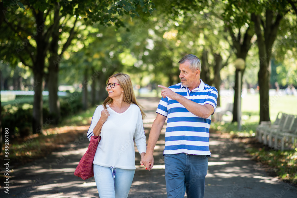 Portrait of happy senior couple walking outdoors in city or town park.