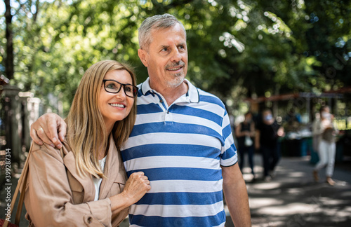 Portrait of happy senior couple standing outdoors in city or town park.