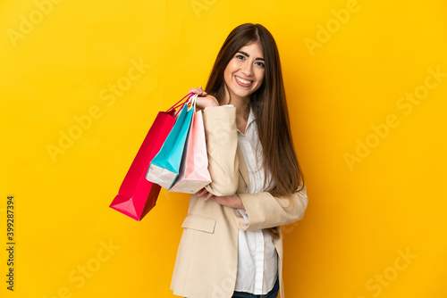 Young caucasian woman isolated on yellow background holding shopping bags and smiling