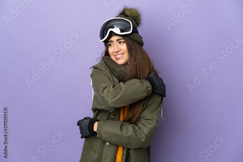Skier caucasian girl with snowboarding glasses isolated on purple background suffering from pain in shoulder for having made an effort © luismolinero