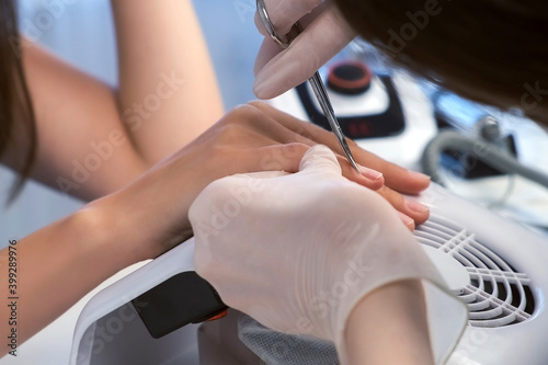 Classical manicure. Hygiene and care for hands, beauty industry concept. Woman manicurist master is cutting cuticle using scissors on client's finger in beauty salon, closeup hands view.