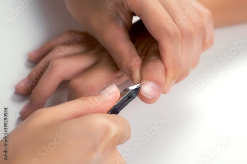 Woman is cutting skin around nail on teenager boy hand using nail tongs  hands closeup. Cuts off the burrs near the nails on white background. Hygiene procedure and care for hands.