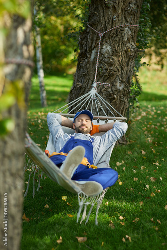 Fotografía Peaceful young workman wearing uniform taking a break, lying in a hammock outdoo