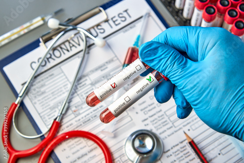 Test tubes in the doctor's hand with blood tests for COVID-19 on the background of the analysis form. Blood test for the presence of antibodies to the causative agent of a new coronavirus infection.