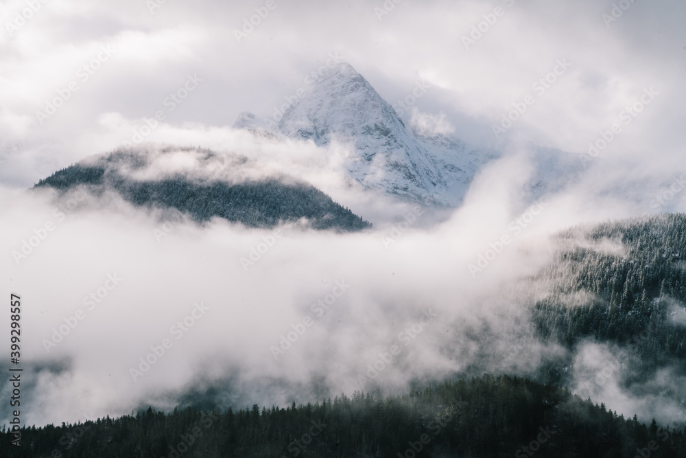 Snowy mountain peak in hillside terrain with foggy coniferous forest