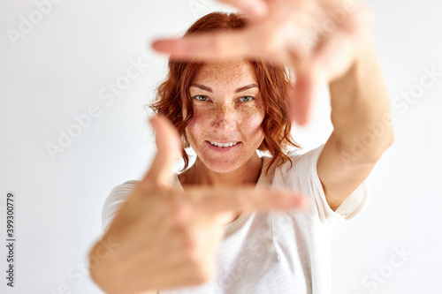 redhead optimistic female pretend to take photo, make shape of square as camera from hands, smile isolated over white background
