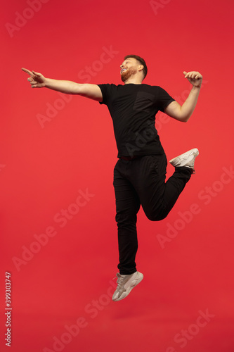 Pointing. Full length portrait of young successfull high jumping man gesturing isolated on red studio background. Attractive male caucasian model. Copyspace. Human emotions, facial expression concept. © master1305