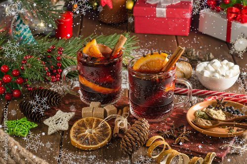 Mulled wine with orange slice, cinnamon stick on wooden background with falling snowflakes © Victoria