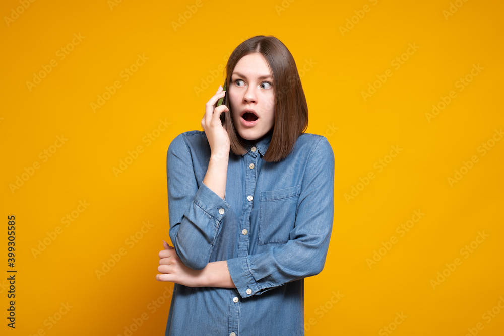 Young casual surprised woman during a phone call, stands on a yellow background. Young casual surprised woman during a phone call, stands on a yellow background.
