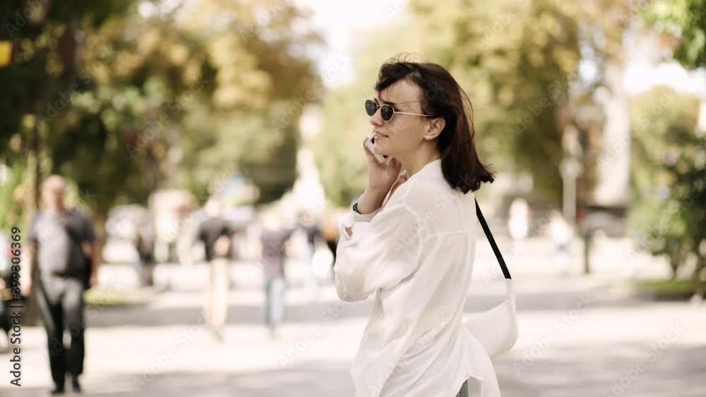 Girl emotionally walks and turns around and looks at camera. Young woman walking in the street, talking nicely on the phone and smiles, enjoys a conversation with her beloved or friend. Girl emotionally walks and turns around and looks at camera. Young woman walking in the street, talking nicely on the phone and smiles, enjoys a conversation with her beloved or friend.