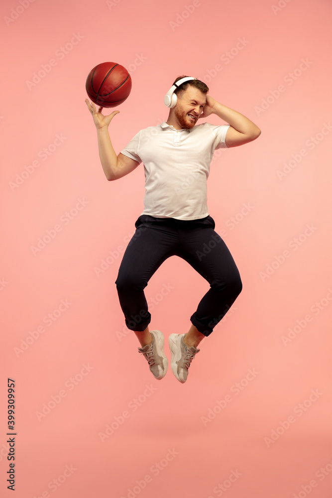 Basketball player in action. Full length portrait of young high jumping man isolated on pink studio background. Male caucasian model. Copyspace. Human emotions, facial expression, sport concept.