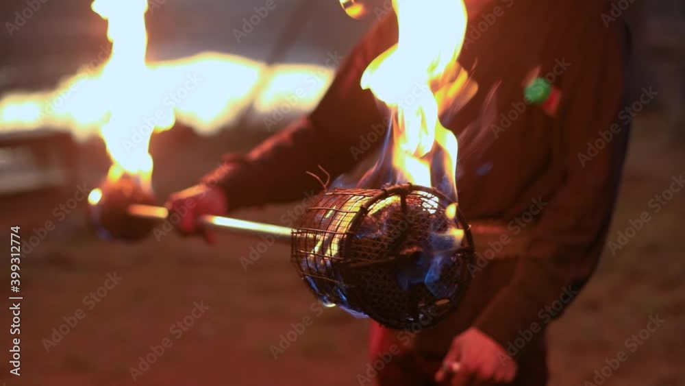Selective focus of young male hands lighting net on fire stick using lighter while preparing for performance during fire jamming