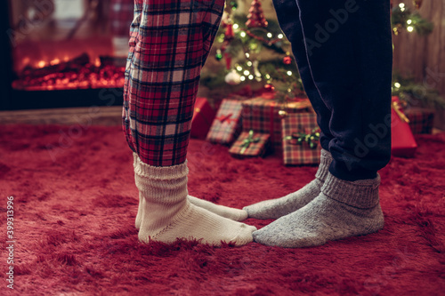 Woman feet standing in tip toe in winter socks on male lags on a fluffy red blanket near a Christmas tree with gifts. Concept