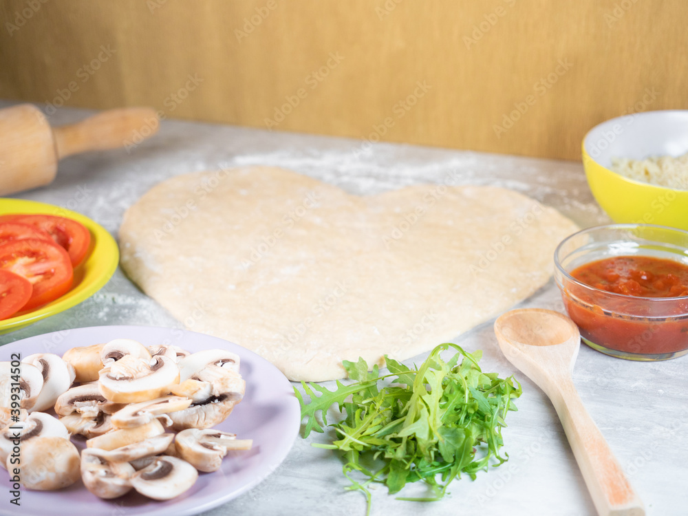 Heart shape pizza dough and ingredients on the table Heart shape pizza dough and ingredients on the table