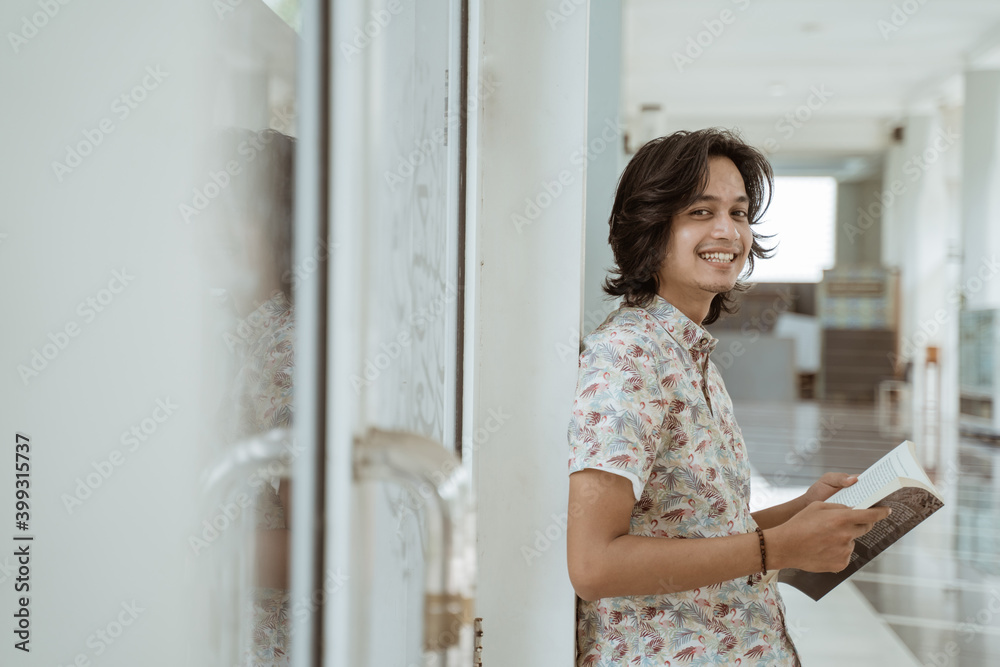 Portrait of happy male student holding book and looking at camera on campus. Portrait of happy male student holding book and looking at camera on campus.
