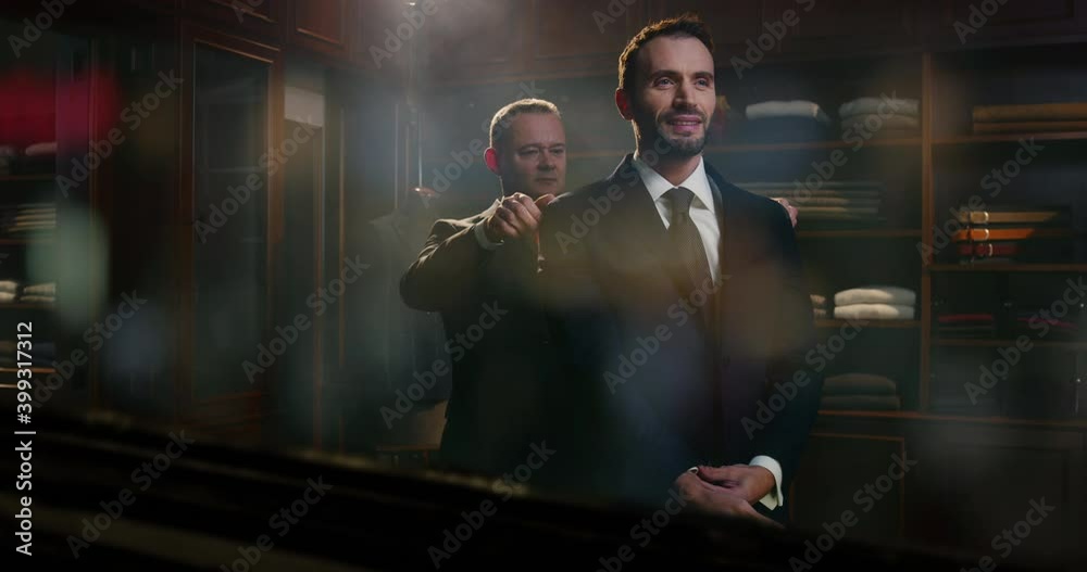 Cinematic shot of businessman is trying new high quality tailored suit with designer in luxury atelier with passing people reflection on shop window. Concept of fashion, couturier,city center,business