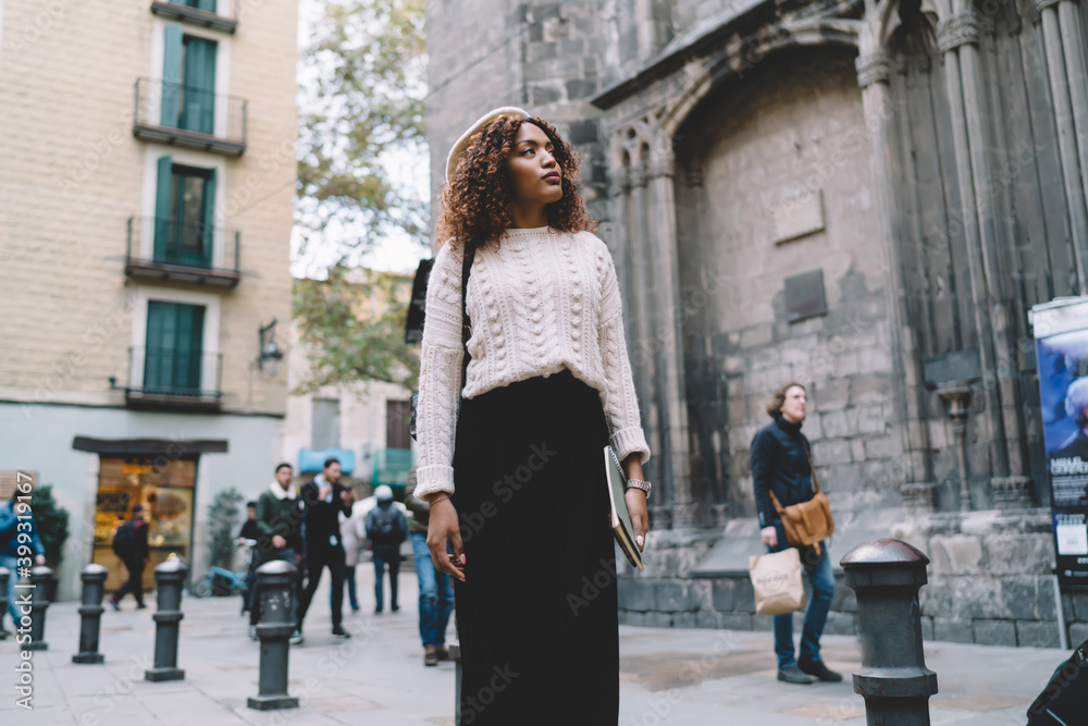 Beautiful african american hipster girl traveler in trendy wear explore location and destinations in city, charming dark skinned woman 20s looking at town and architecture on leisure in town
