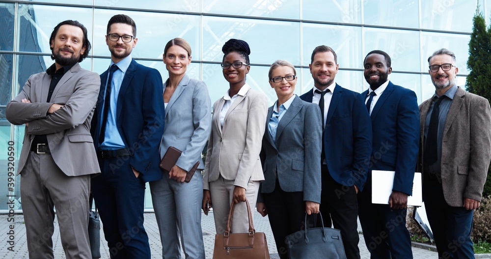 Obraz premium Portrait of mixed-races businessmen and businesswomen standing together outdoors and smiling to camera. Multi ethnic team of business males and females partners. International group of investors.