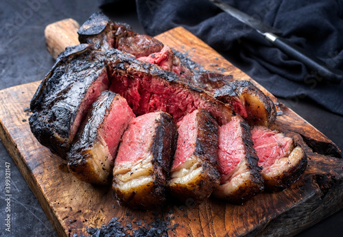 Traditional barbecue dry aged wagyu t-bone beef steak bistecca alla Fiorentina sliced and served with black salt as close-up on an old rustic wooden board