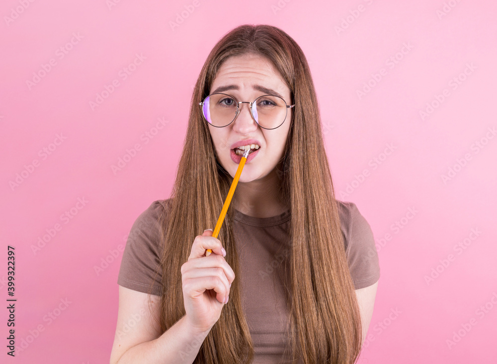 Portrait of thoughtful girl having pencil in mouth, looking to camera isolated on pink background. Portrait of thoughtful girl having pencil in mouth, looking to camera isolated on pink background.