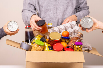 Volunteers hands collecting grocery products, foodstuff to food donations box