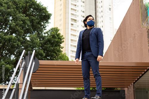 Homem em paisagem urbana, usando blazer e máscara de proteção contra covid-19.