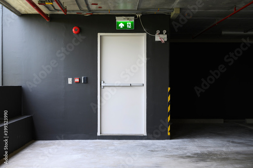 Fotografia A fire exit with the sign and red alarm bell above the white door on the parking building