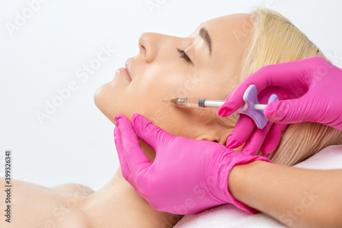 Cosmetologist makes rejuvenating anti wrinkle injections on the face of a beautiful blonde woman. Female aesthetic cosmetology in a beauty salon.