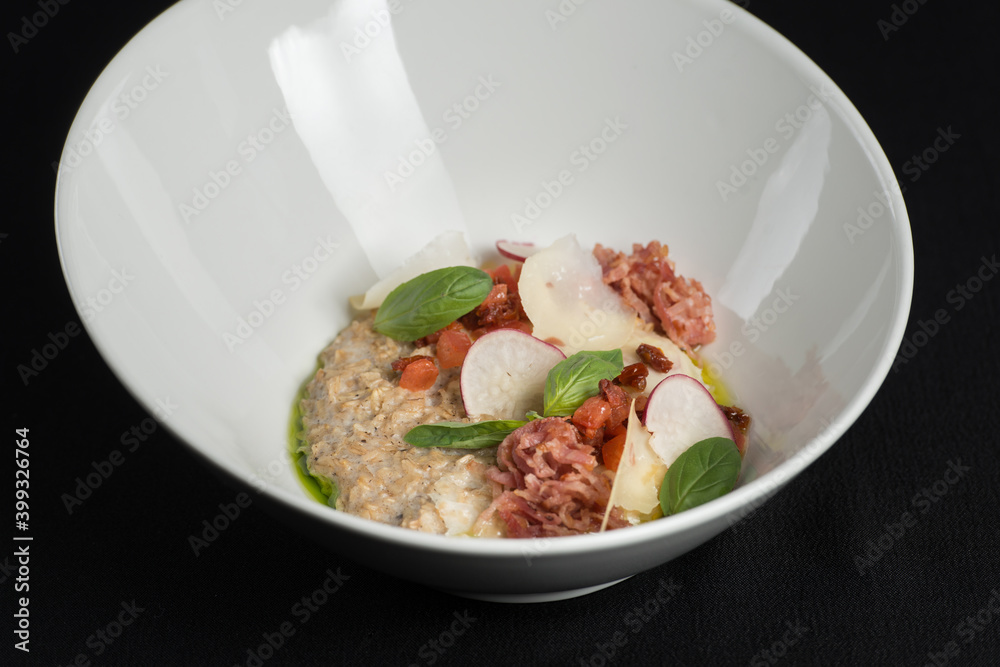 Delicious salted oatmeal, bacon and vegetables on a black tablecloth Delicious salted oatmeal, bacon and vegetables on a black tablecloth