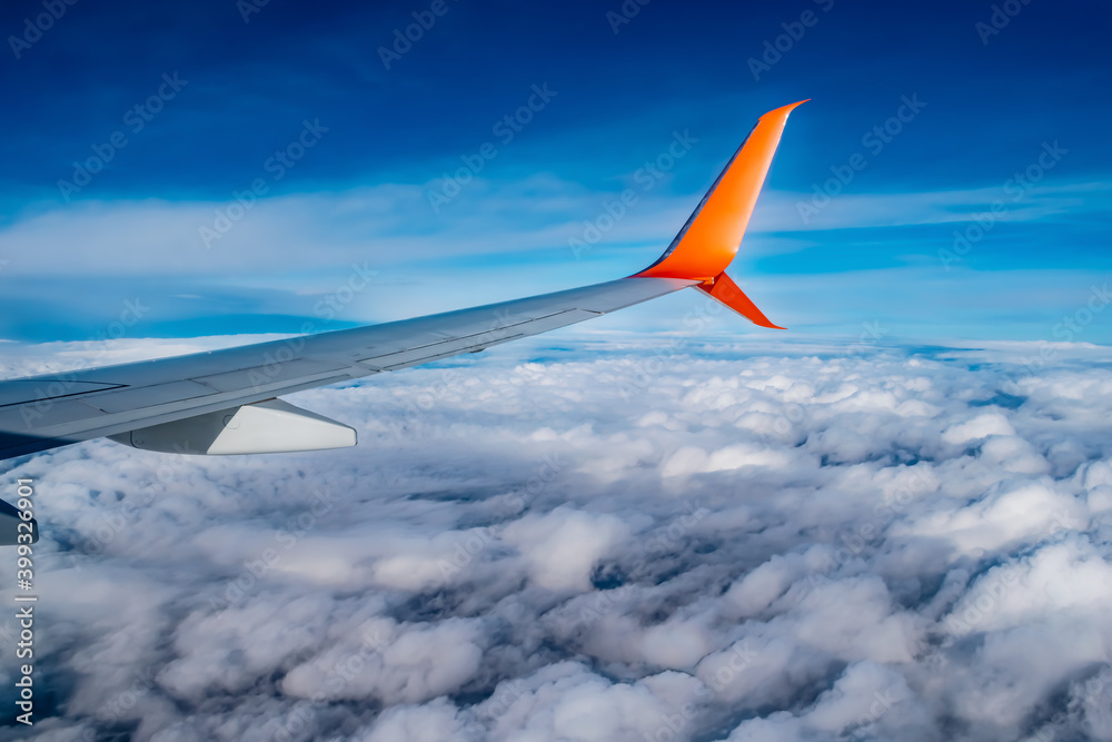 Airplane wing in blue sky above white fluffy clouds. Passenger transport flies in the atmosphere against the backdrop of a natural landscape Airplane wing in blue sky above white fluffy clouds. Passenger transport flies in the atmosphere against the backdrop of a natural landscape