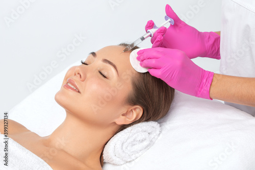 Cosmetologist makes rejuvenating anti wrinkle injections on the face of a beautiful brunette woman. Female aesthetic cosmetology in a beauty salon.