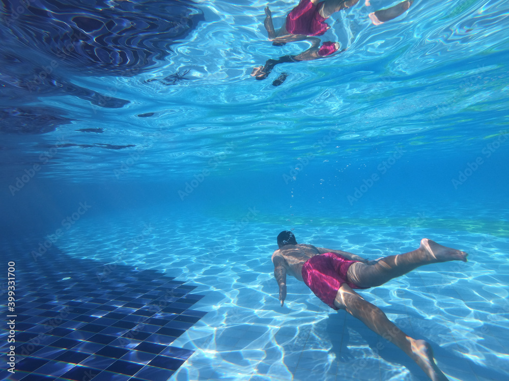 Young man swimming underwater in the pool