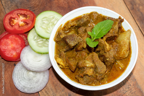Traditional homemade Bengali style spicy dish mutton curry or lamb curry in a white bowl with salad on wooden background.