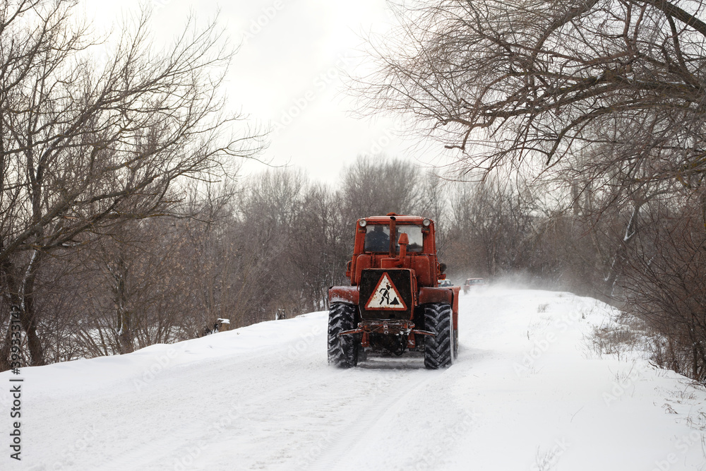 Old tractor clears the snow-covered road from snow blockages